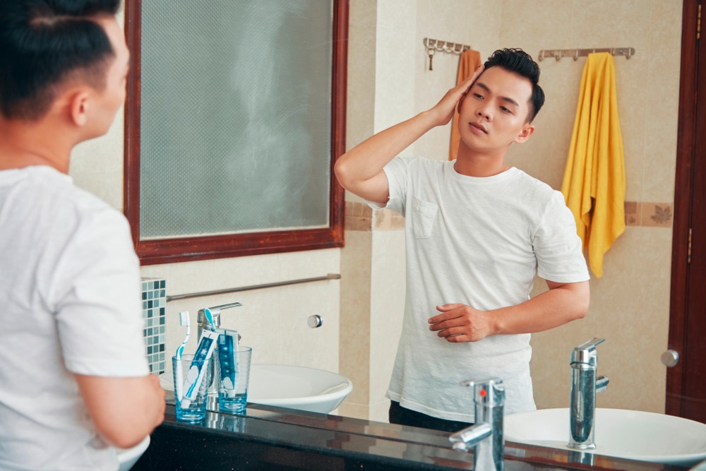 Man styling his hair with his hand in front of the mirror.