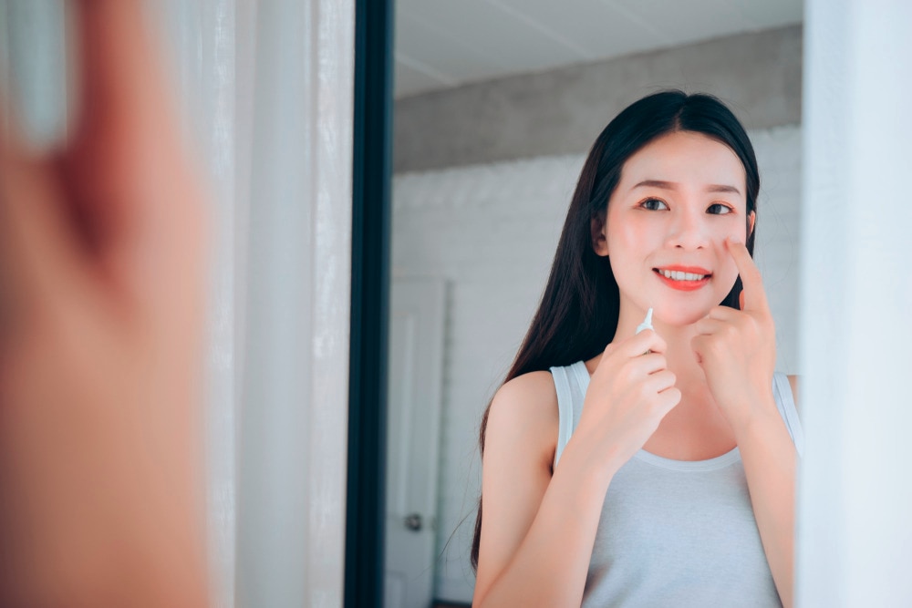 Asian woman looking at the mirror, touching her face.