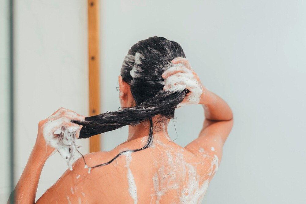Woman washing her long hair with shampoo in the shower.