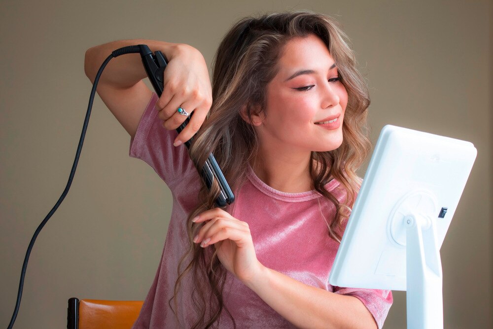 Woman curling her long hair with a curling iron.