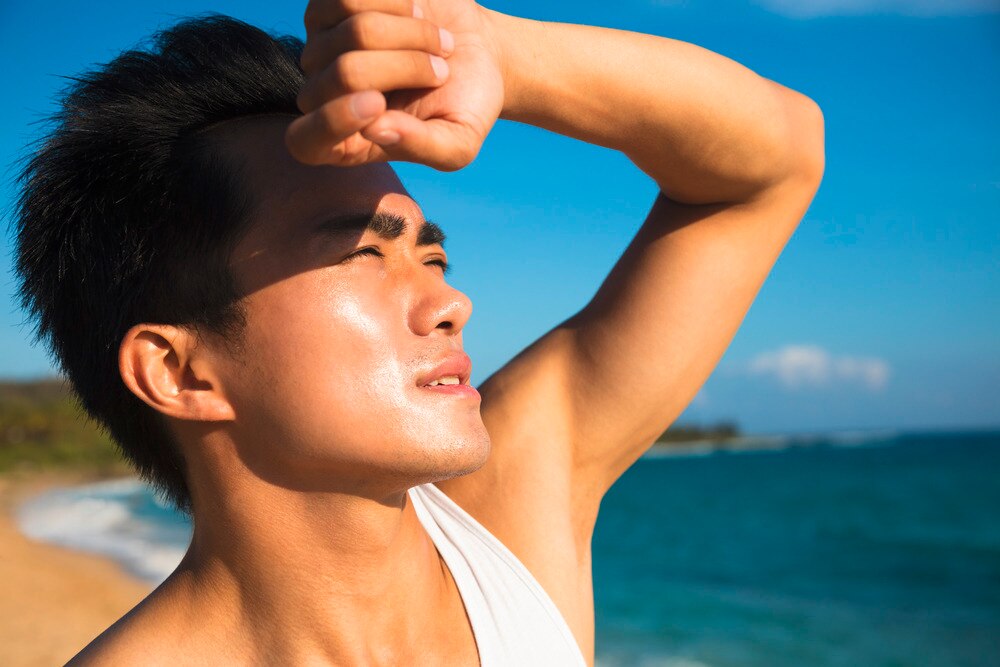 A portrait of man covering his eyes with his arm on the beach.