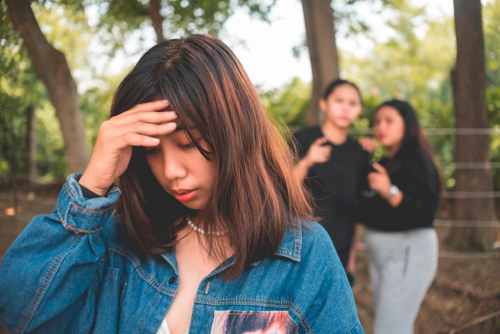 Woman touching her forehead in shame while two other women gossiping behind her.