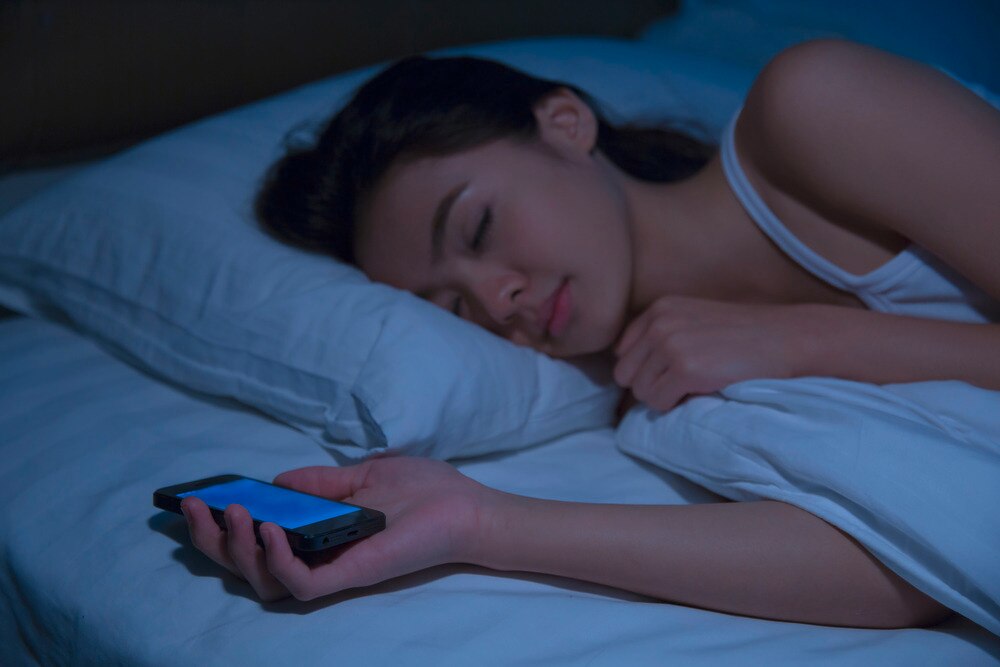 Asian woman sleeping in bed while holding phone.
