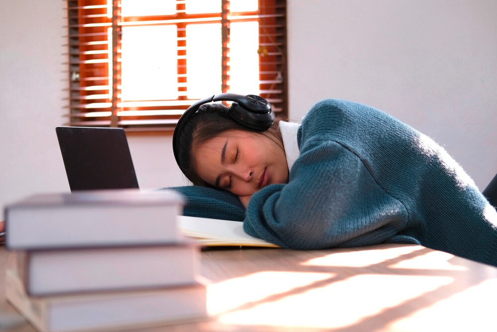 Asian woman with headphones sleeping in front of laptop.