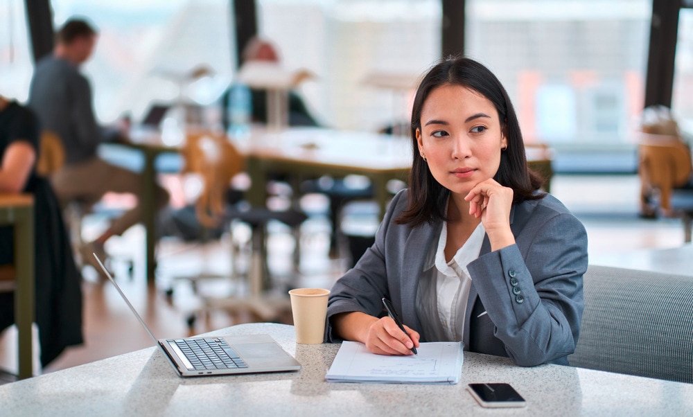 Asian woman in tailored suit sitting in front of laptop at work.