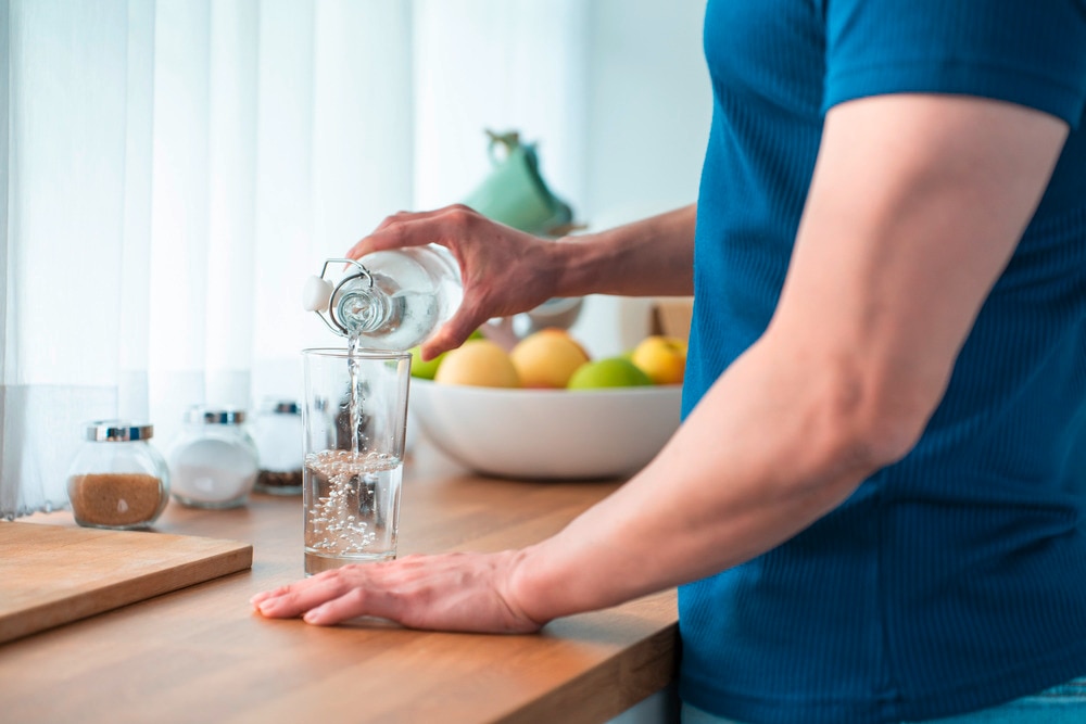 Closeup of a man’s hands pouring water into a glass.