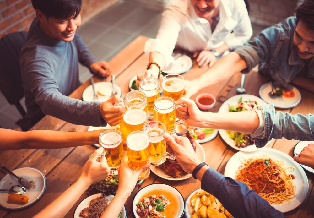 A group of men clinking glasses of beer over a dining table.