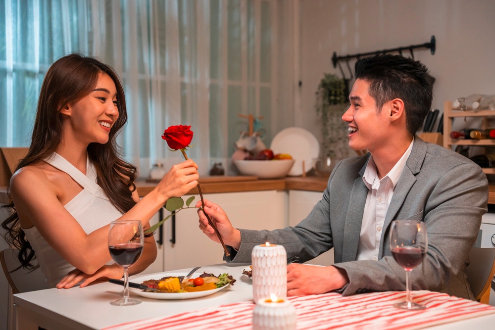 Asian man giving red rose to woman on dinner date.