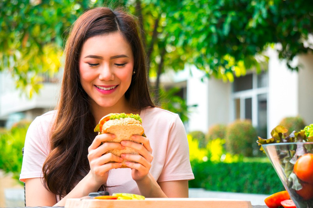 Woman eating sandwich at a park.