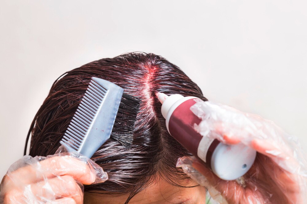 Woman applying hair color chemicals on her roots with a brush.