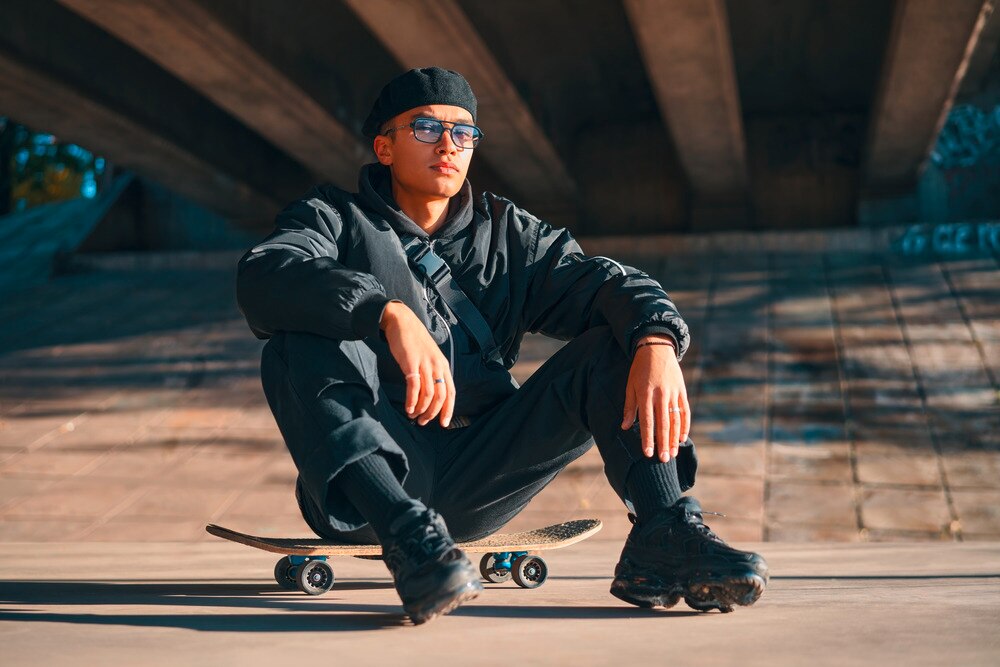 A portrait of man in all black outfit sitting on a skateboard.