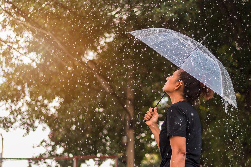 Asian girl in black shirt looking up at rain with clear umbrella.