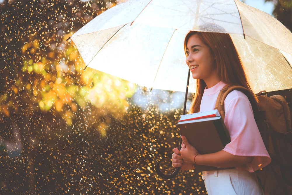 Smiling Asian woman with books under umbrella.