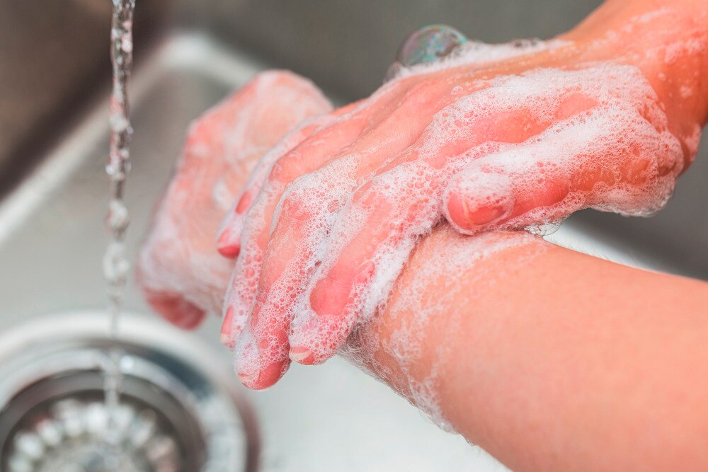 Close up of hands with soap and water by a sink.