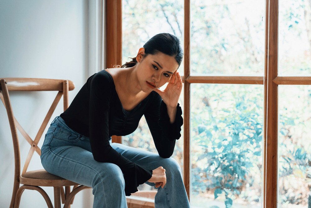 A portrait of woman with sad expression sitting on a chair.