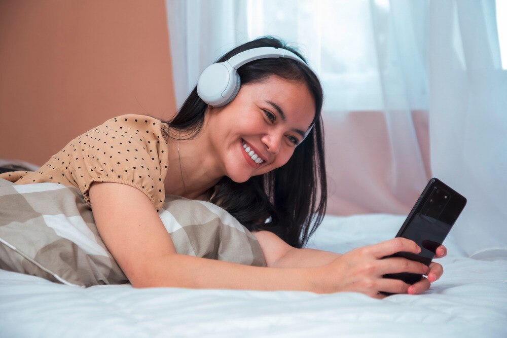Woman with white headphone smiling while holding a mobile phone.
