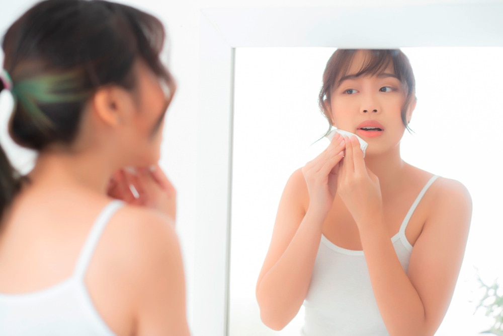 Asian woman cleansing her skin in front of mirror.