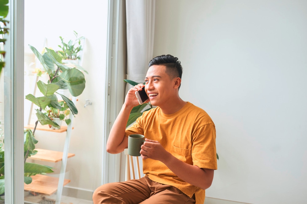 Asian man on the phone while having coffee at home.