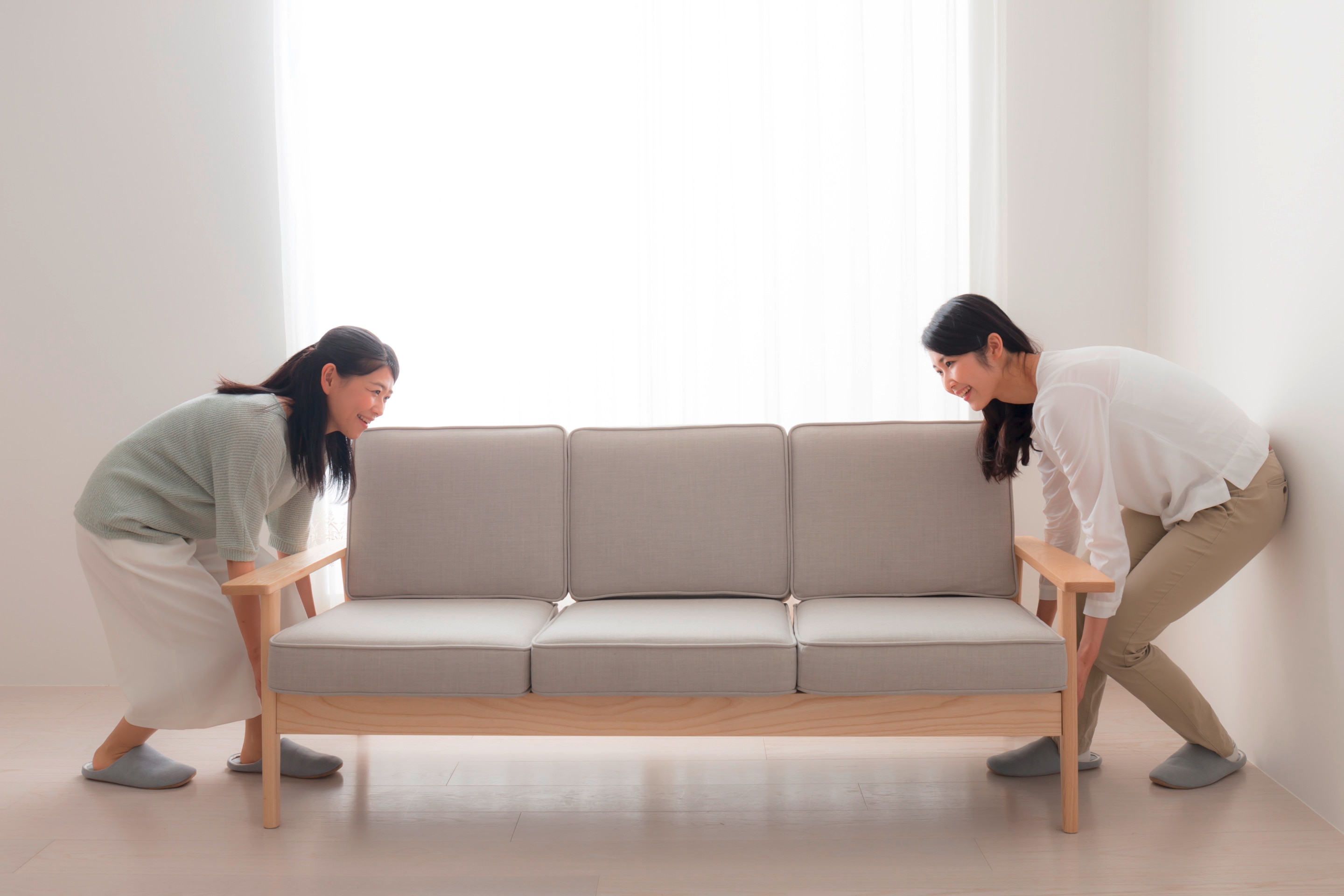 A portrait of two women lifting sofa together.