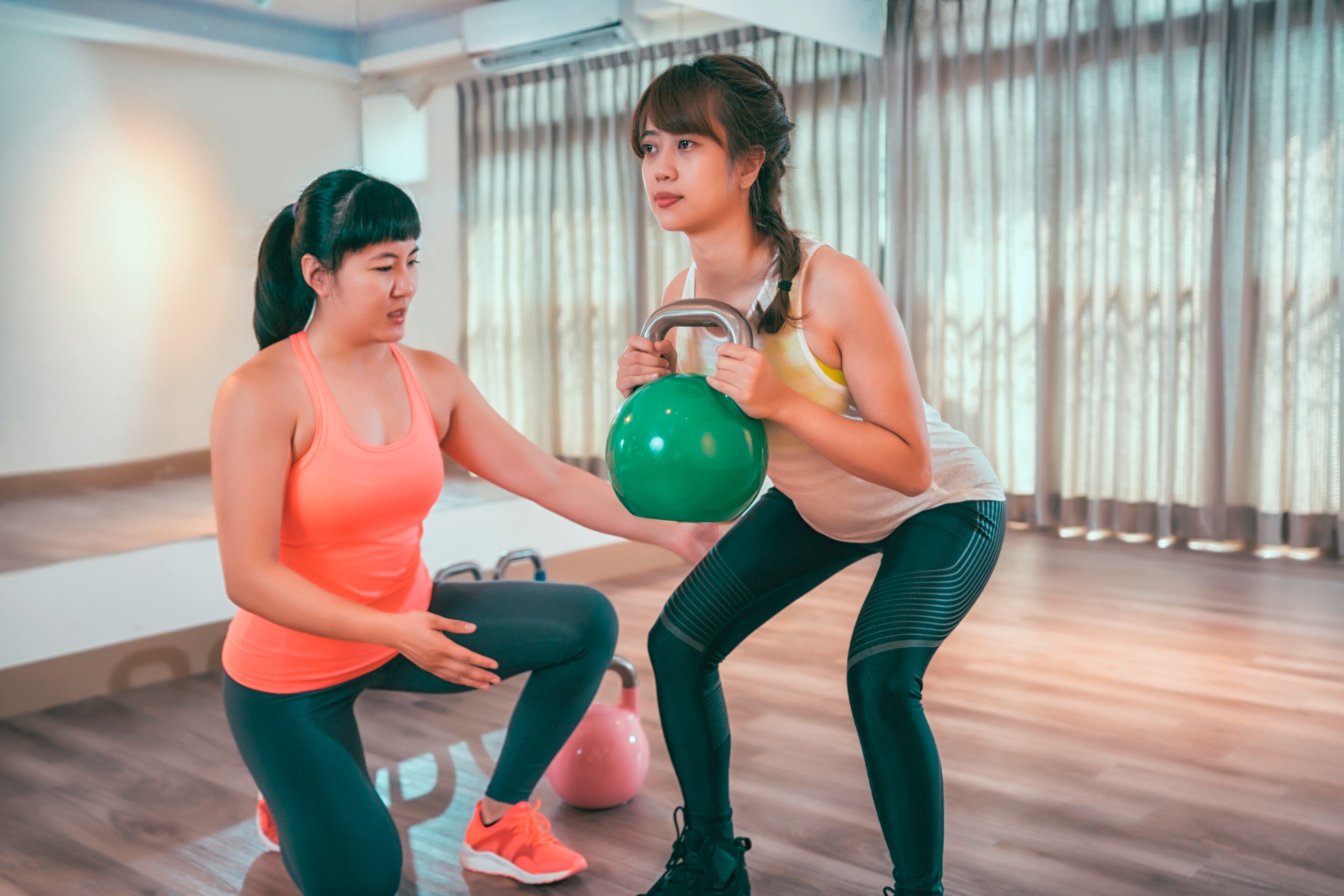 A portrait of gym trainer guiding a woman on how to squat with free weights.