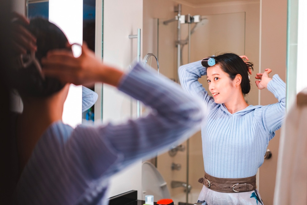 A portrait of woman using hair roller to style her bangs.