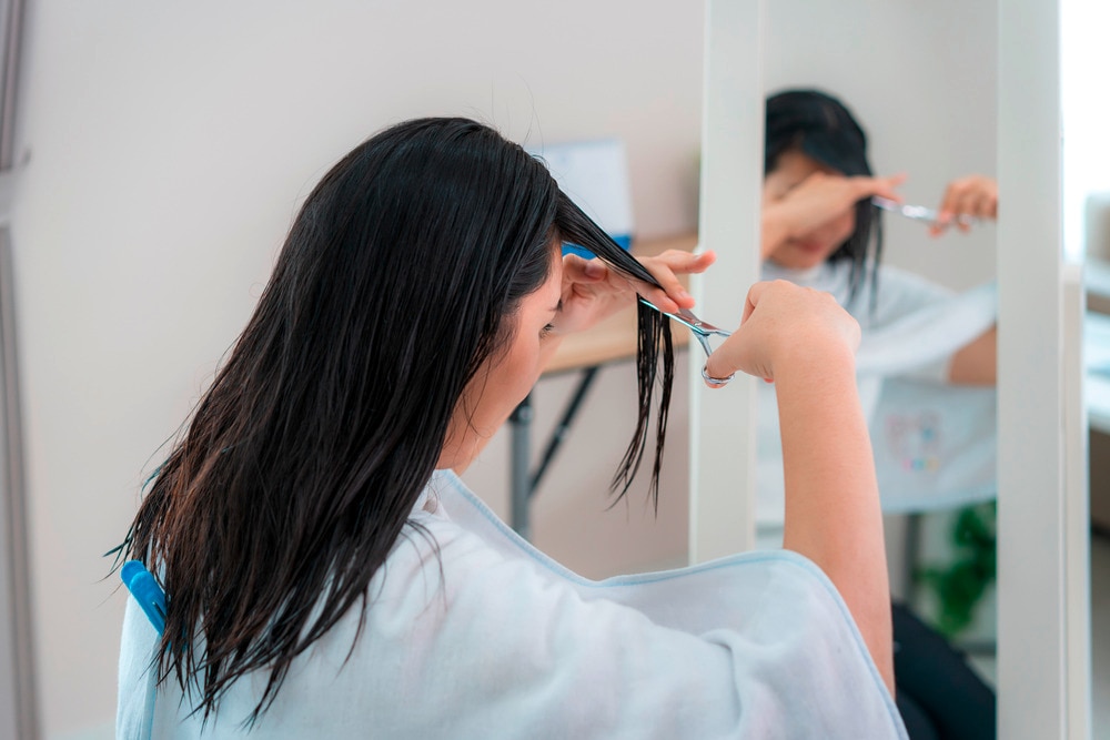Woman cutting her own bangs with scissors at home.