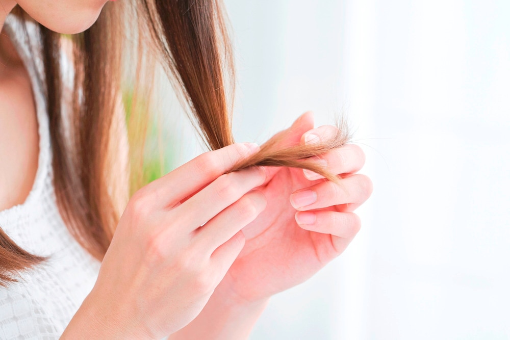 Woman checking the ends of her dry, brittle hair.
