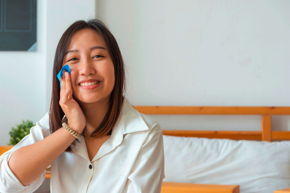 Smiling woman dabbing her cheek with blotting paper.