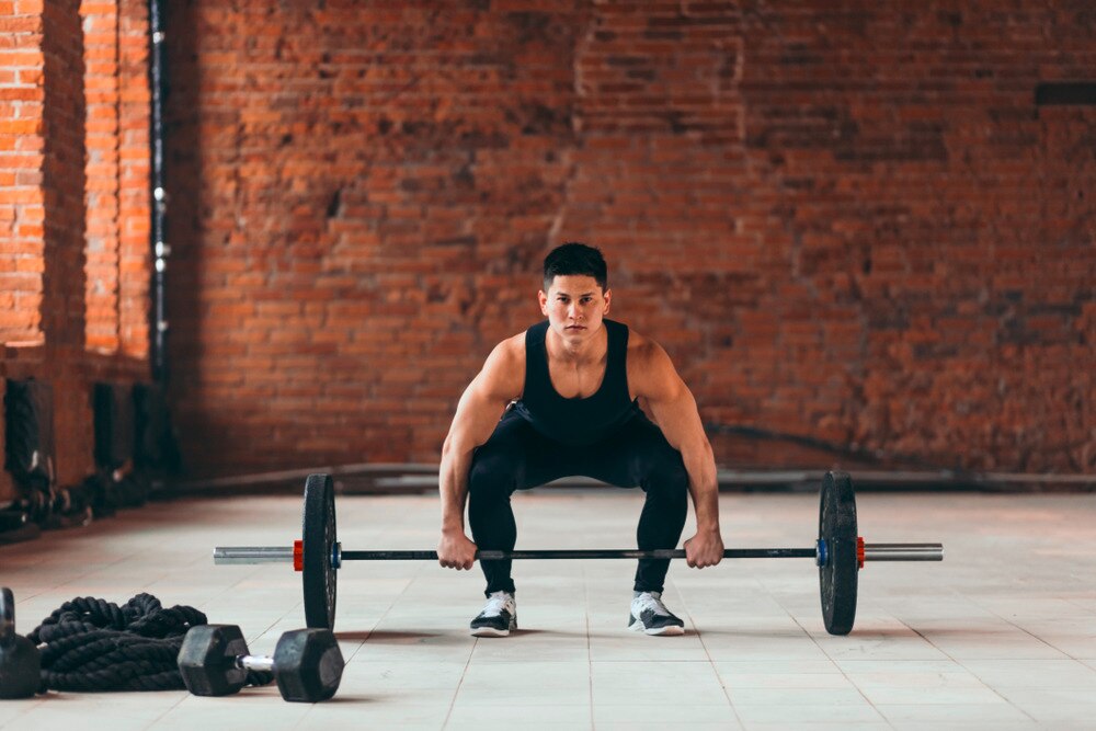 A portrait of man in a deadlift form gripping onto a barbell.