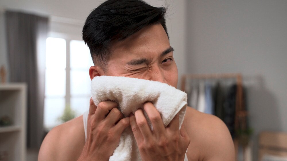 Asian man rubbing face with towel.