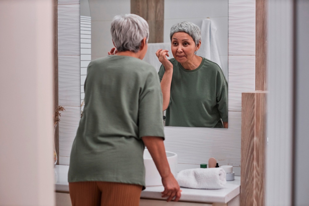 A portrait of woman with gray hair applying cream to her face.