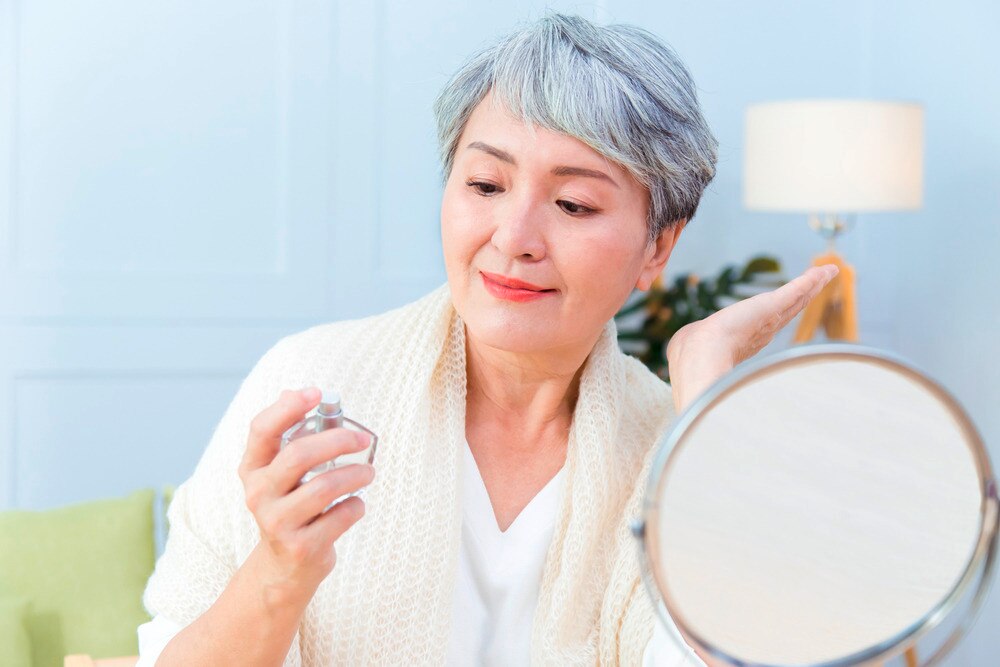 A portrait a senior woman looking at a perfume bottle.