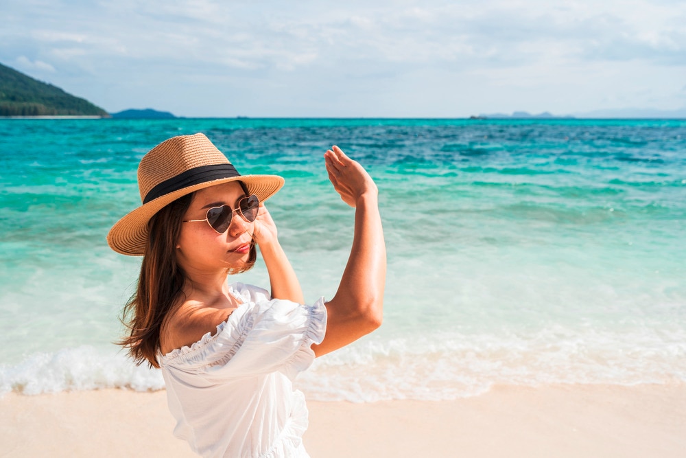 Woman wearing fedora at the beach shielding face from the sun. 
