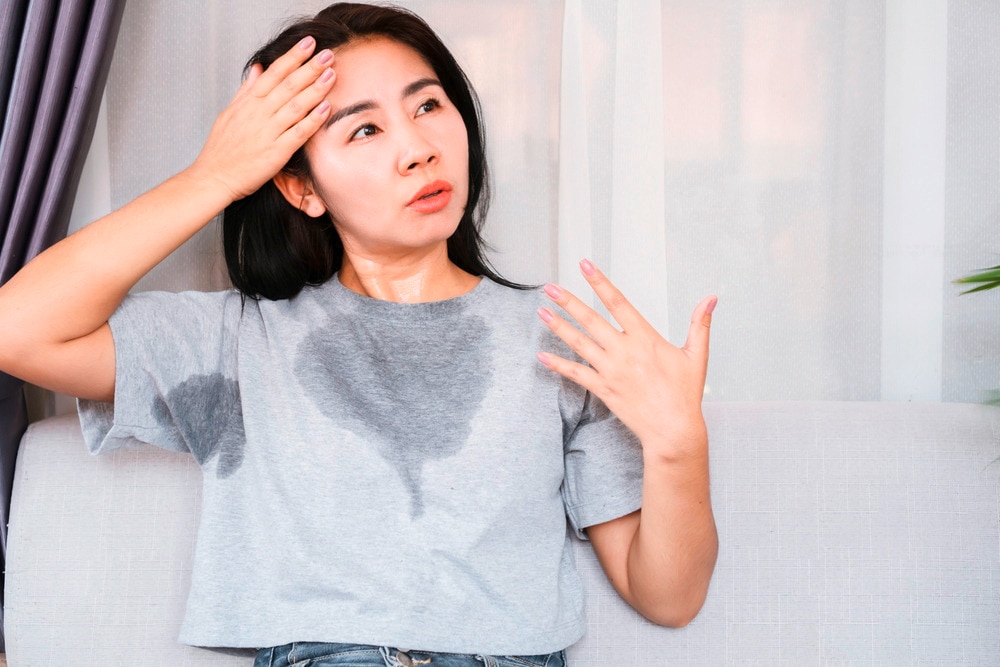 A portrait of woman sweating profusely through her shirt.