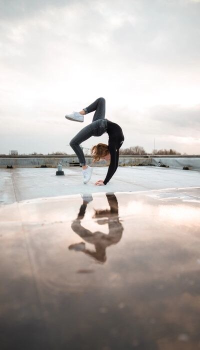 Une femme en jean et t-shirt noir à manches longues fait un pont acrobatique sur un toit plat