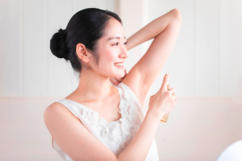 A portrait of woman applying deodorant on her underarm.