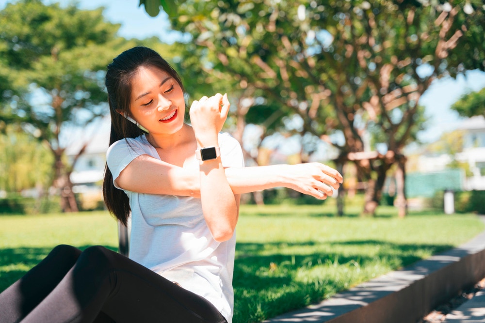 Woman doing arm stretches while sitting on grass.