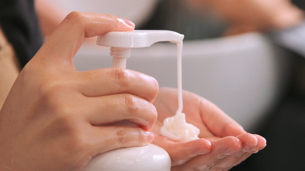 Closeup of a woman’s hand pressing pump bottle of conditioner.