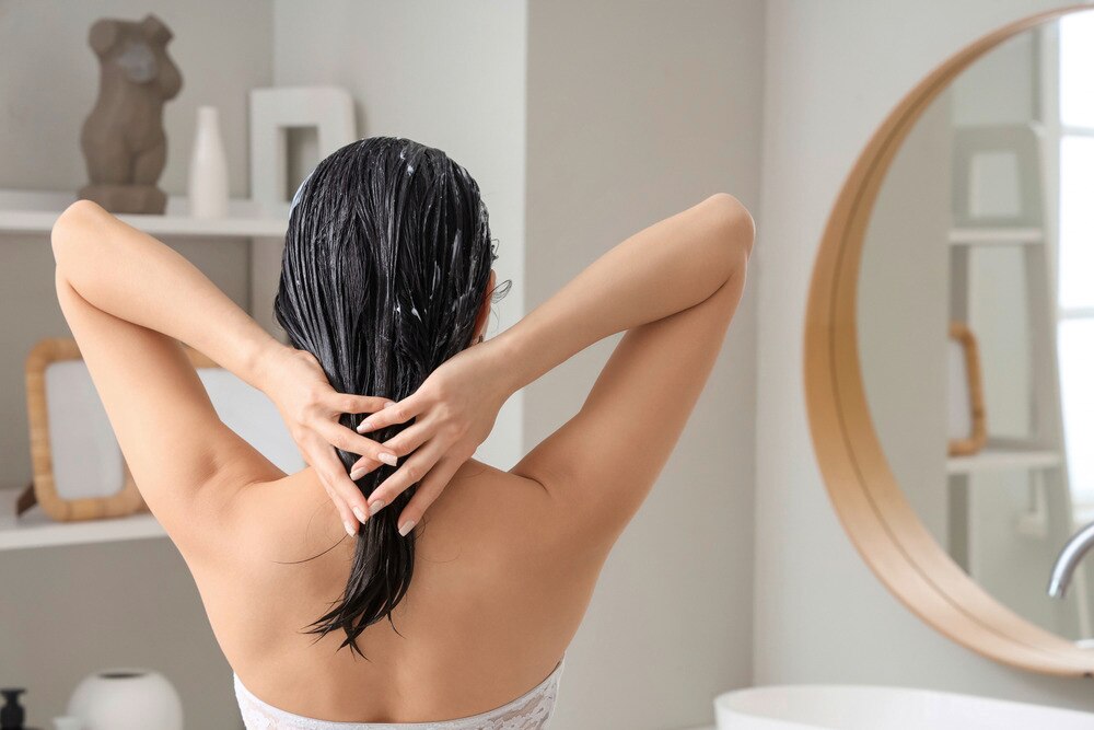 Back of an Asian woman applying hair conditioner.