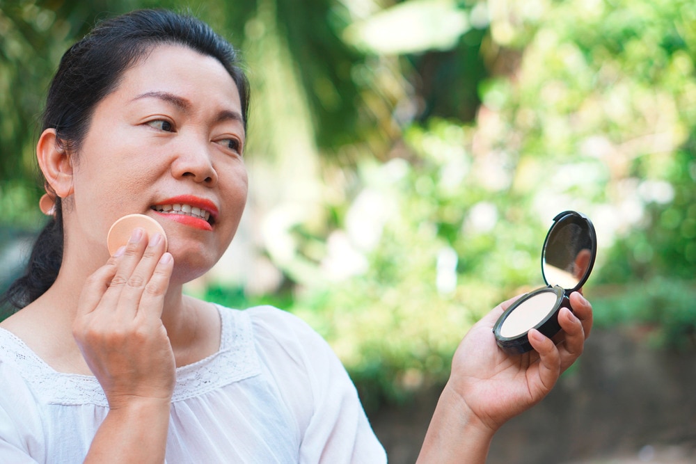 A portrait of woman applying base makeup with a beauty sponge.
