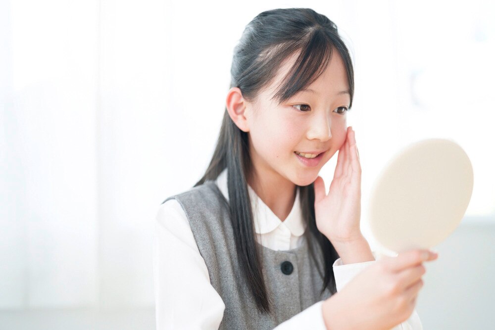 Young Asian girl checks her skin in the mirror.