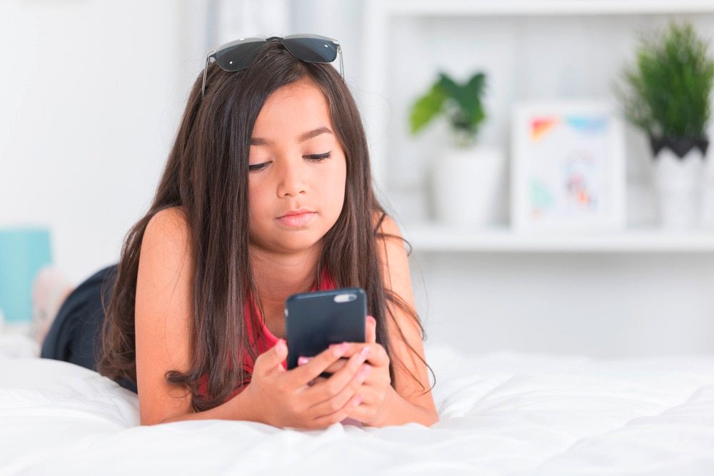 Tween looks at her phone while lying on the bed.