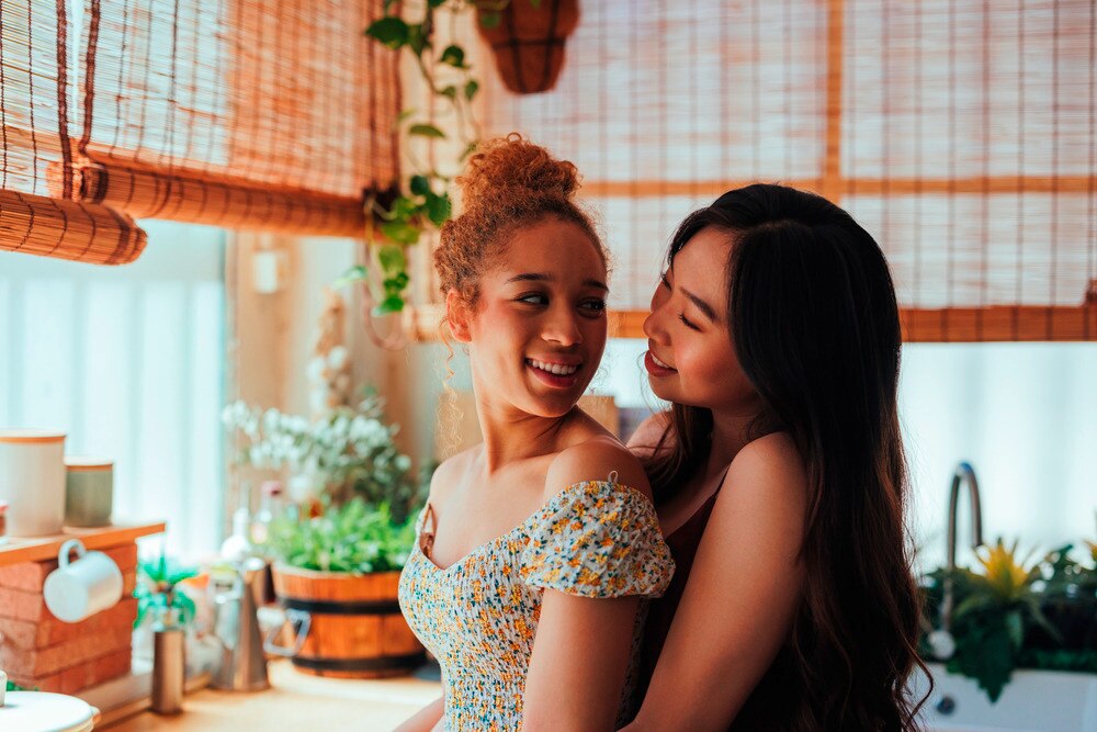 A portrait of two women hugging each other in the kitchen.