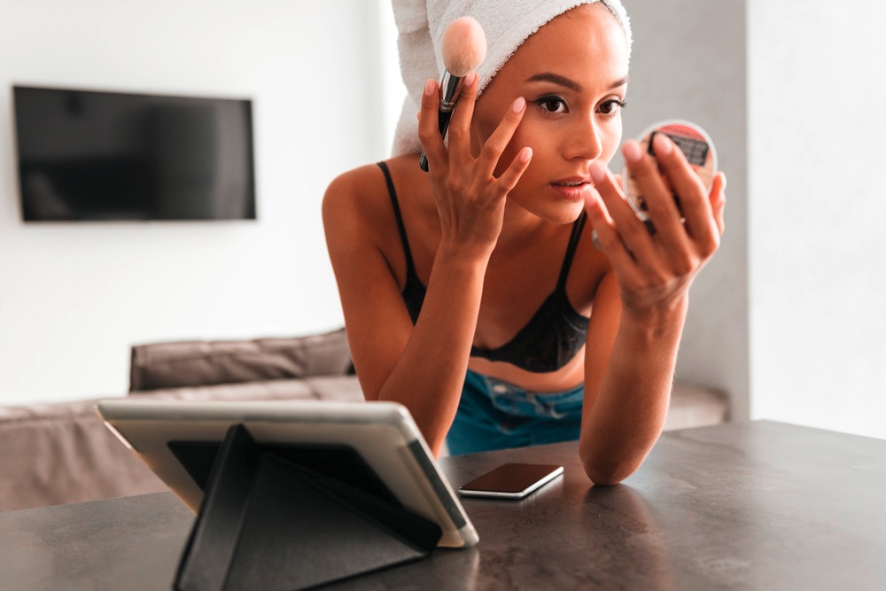 Woman doing her makeup on a kitchen counter.