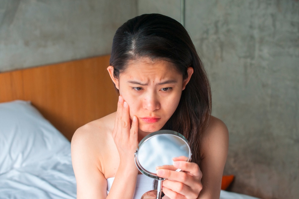 Woman looking at her face in the mirror with a sad expression.