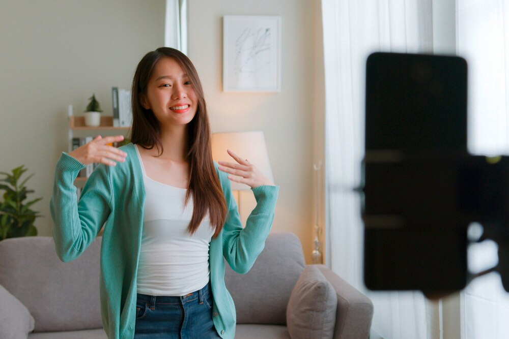 Woman in light blue cardigan dancing in front of a phone.