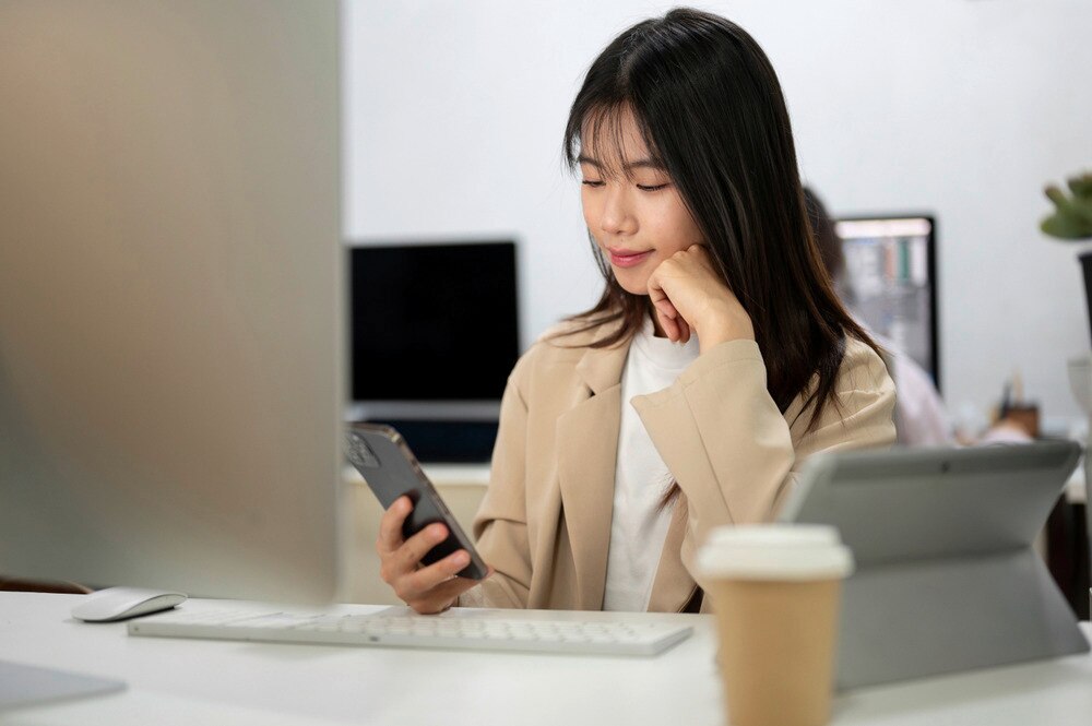Woman in business attire looking at her phone while in an office.