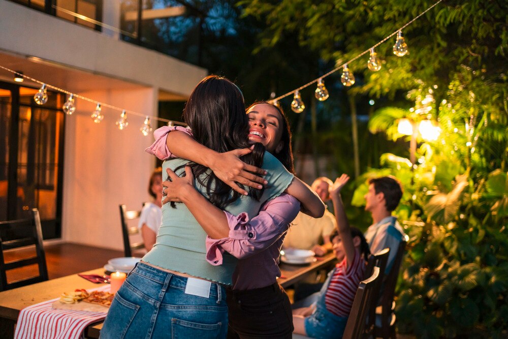A portrait of two women hugging while at a family gathering.