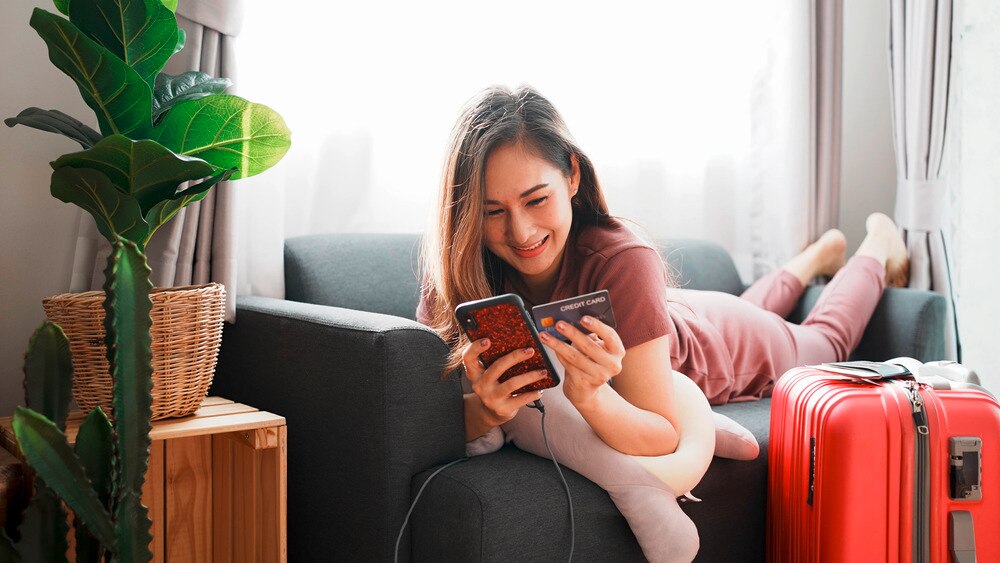 Asian woman on couch holding phone and credit card.