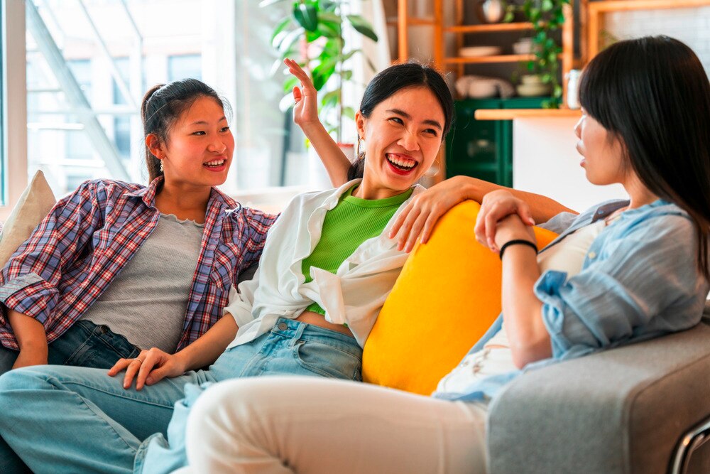 Three Asian women chatting and laughing on sofa.